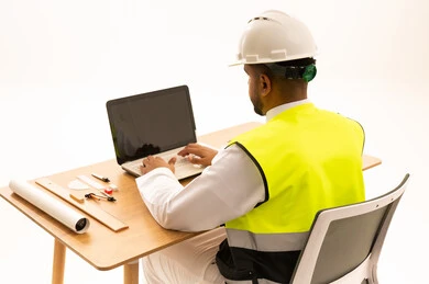 مهندس عربي يرتدي الثوب والخوذة يعمل على الحاسوب المحمول