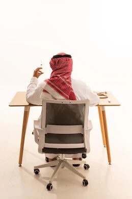 طبيب سعودي يحمل حقنة طبية على مكتبه من الخلف بخلفية بيضاء