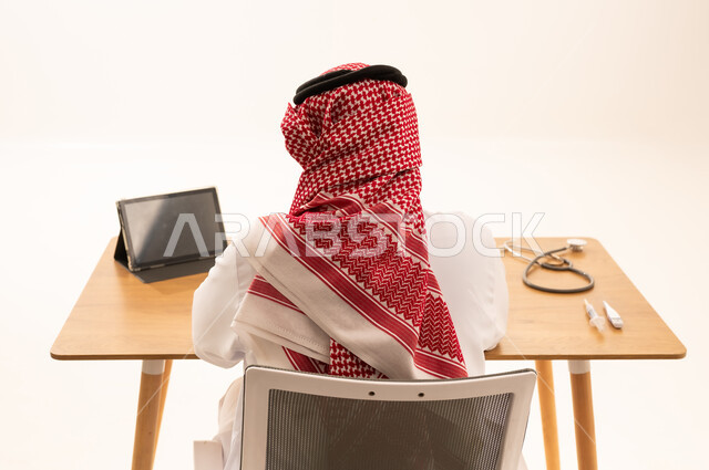 طبيب سعودي يرتدي الزي التقليدي خلف مكتبه مع أدوات طبية