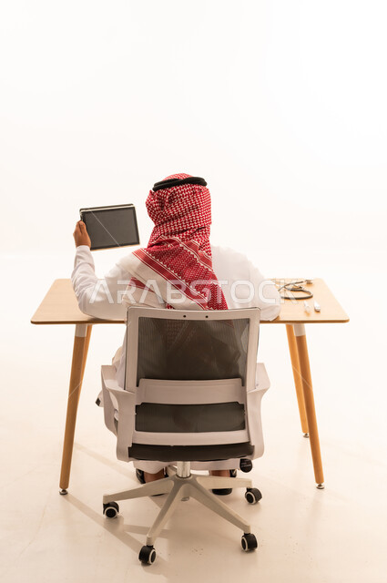 طبيب سعودي يمسك جهاز لوحي في المكتب من الخلف