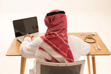 Saudi Doctor Using Laptop at Desk with Stethoscope