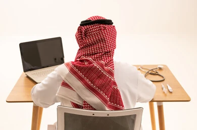 Saudi Male Doctor at Desk with Laptop Back View