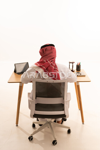 رجل سعودي بالزي التقليدي يعمل خلف مكتبه من الخلف