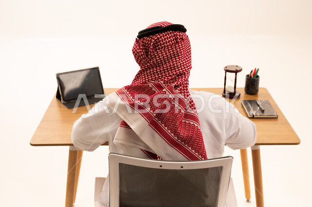 رجل سعودي في مكتب العمل مع جهاز لوحي وساعة رملية