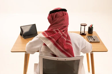 رجل سعودي في مكتب العمل مع جهاز لوحي وساعة رملية