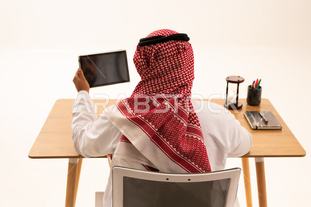 رجل أعمال سعودي خلف مكتبه يحمل جهاز لوحي