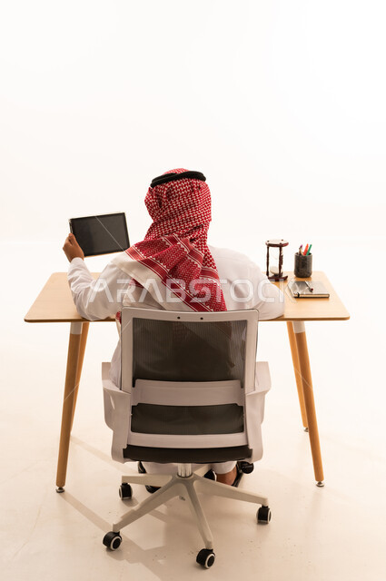 رجل أعمال سعودي بالثوب التقليدي يعمل خلف مكتب خشبي