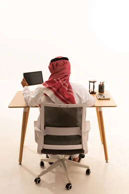 رجل أعمال سعودي بالثوب التقليدي يعمل خلف مكتب خشبي