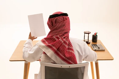رجل سعودي بالزي التقليدي يمسك ورقة بيضاء في المكتب