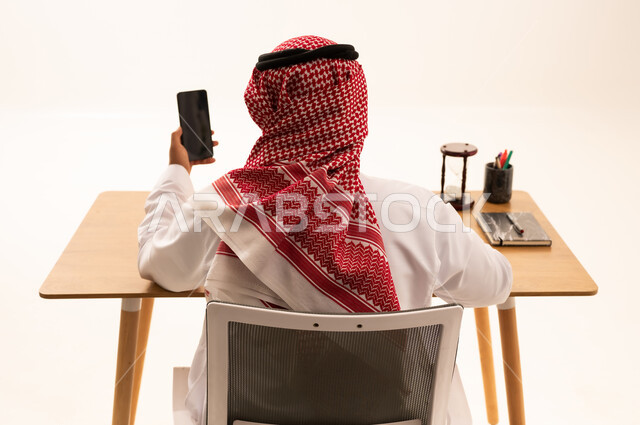 رجل سعودي في المكتب يحمل هاتف ذكي من الخلف