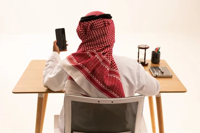 Saudi Man at Office Desk Holding Smartphone Rear View