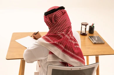 Saudi Man in Traditional Dress Writing at Office Desk