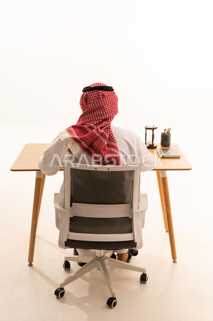 رجل أعمال سعودي يعمل على مكتبه من الخلف