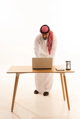 Saudi Businessman in Thobe Using Laptop at Desk