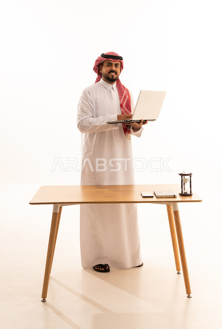 رجل أعمال سعودي بالثوب التقليدي يحمل كمبيوتر محمول