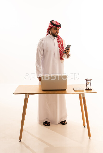رجل سعودي بالزي التقليدي يستخدم الهاتف الذكي في المكتب