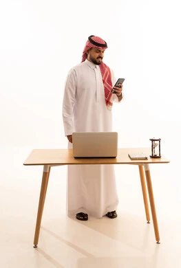 Saudi Man in Traditional Thobe Using Smartphone at Desk