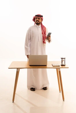 رجل أعمال سعودي مع هاتف ذكي وحاسوب في المكتب