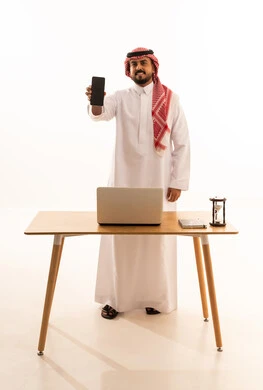 Saudi Man in Thobe Holding Smartphone at Office Desk