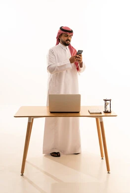رجل أعمال سعودي يستخدم الهاتف الذكي في مكتب أبيض