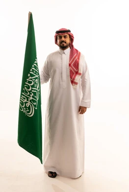 رجل سعودي يمسك بعلم السعودية بالزي التقليدي