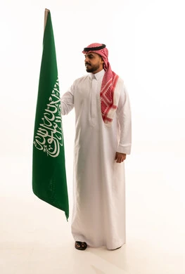 رجل سعودي يحمل العلم الوطني السعودي بخلفية بيضاء
