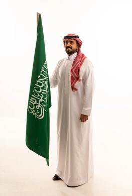 رجل سعودي بالزي التقليدي يحمل علم السعودية