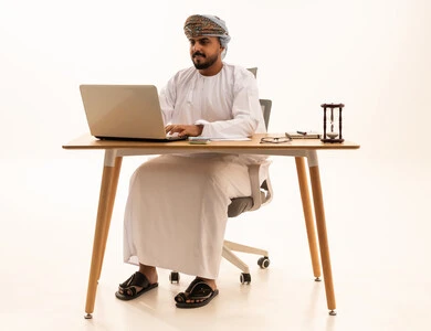 Omani Man in Traditional Dishdasha Using Laptop at Desk