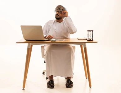 رجل عماني في المكتب مع كمبيوتر وساعة رملية