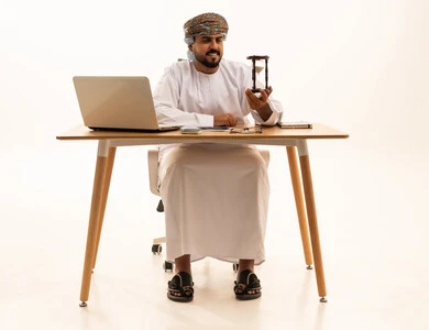 رجل أعمال عماني يحمل ساعة رملية أمام جهاز المحمول