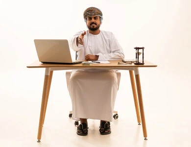 رجل أعمال عماني يصافح خلف مكتب العمل مع حاسوب محمول