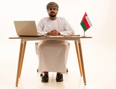 Omani Businessman at Desk with National Flag and Laptop