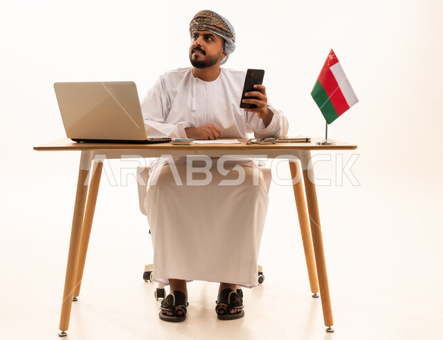 رجل عماني مع لابتوب وعلم عمان على مكتب العمل