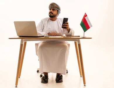 رجل عماني مع لابتوب وعلم عمان على مكتب العمل