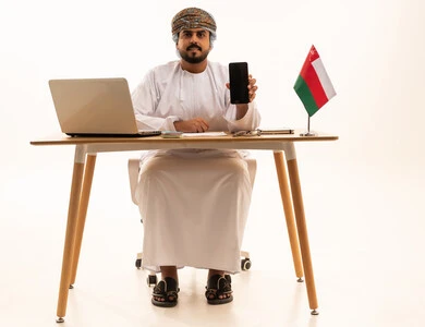 رجل عُماني مع هاتف ذكي وحاسوب محمول على المكتب