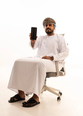 رجل عُماني يحمل هاتفاً ذكياً على كرسي مكتب خلفية بيضاء