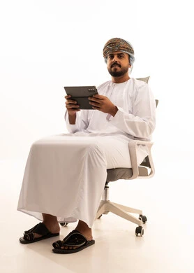 رجل عُماني مع جهاز لوحي على كرسي مكتب بخلفية بيضاء
