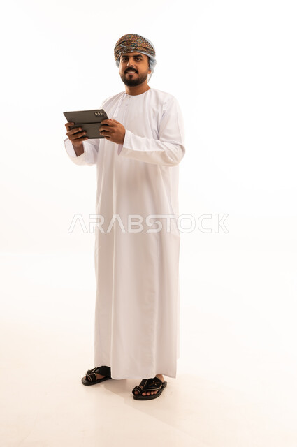 رجل عُماني بالزي التقليدي يستخدم جهازاً لوحياً
