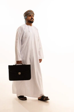 رجل أعمال عماني يسير بحقيبة على خلفية بيضاء