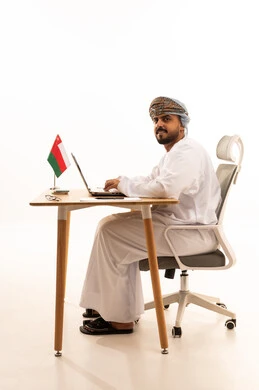 Omani Man Working on Laptop at Desk with National Flag