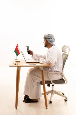 Omani Man Working at Desk with Laptop and Flag