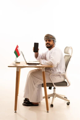 موظف عُماني بالزي التقليدي مع هاتف وكمبيوتر محمول