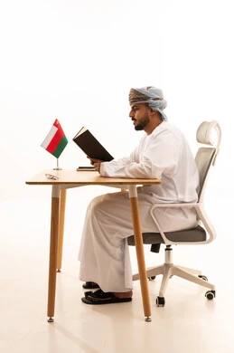 Omani Man Reading Book at Office Desk with National Flag
