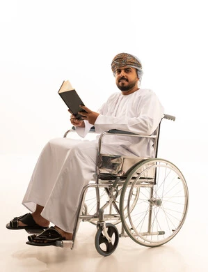 رجل عماني على كرسي متحرك يقرأ كتاباً خلفية بيضاء