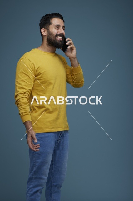 شاب سعودي مبتسم يتحدث بالهاتف الذكي بملابس كاجوال صفراء