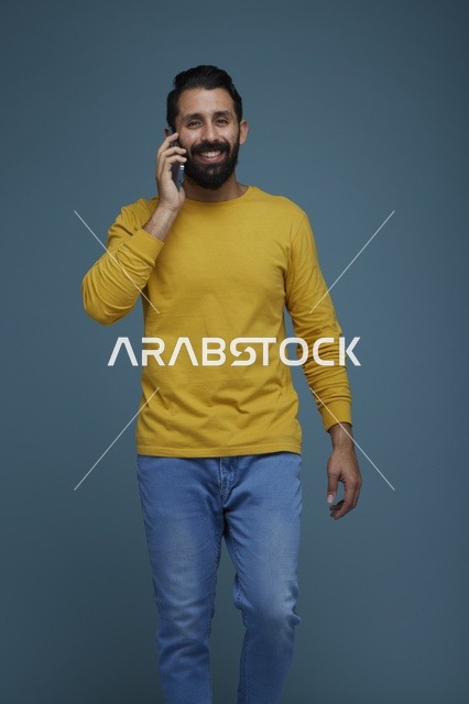 شاب سعودي يتحدث عبر الهاتف الذكي بملابس كاجوال في استوديو