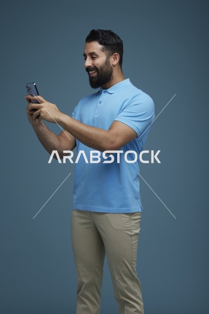 شاب سعودي يستخدم الهاتف الذكي في استوديو بخلفية زرقاء
