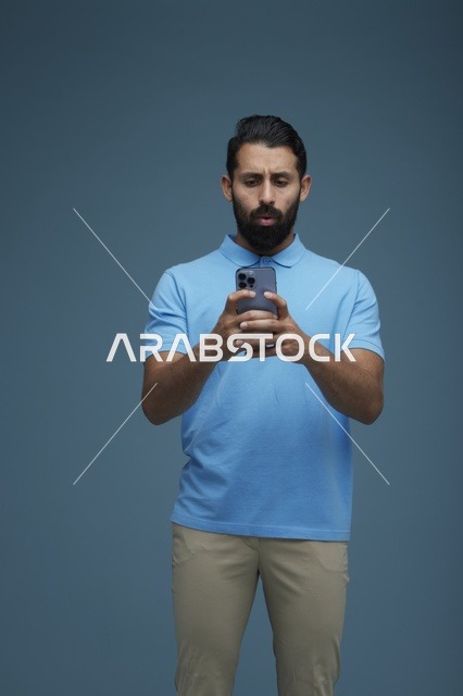 شاب سعودي يستخدم الهاتف الذكي بملابس كاجوال في الاستوديو