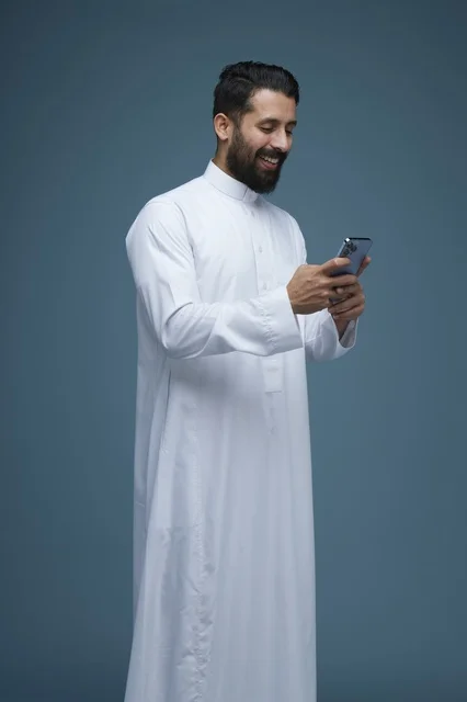 رجل سعودي بالثوب التقليدي يستخدم الهاتف الذكي