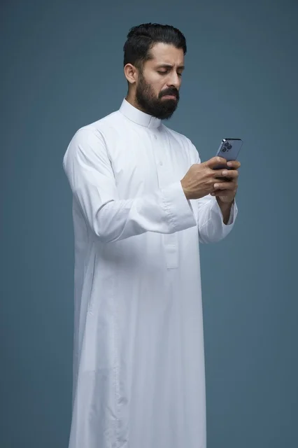 Saudi Man in Traditional Thobe Using Smartphone Studio